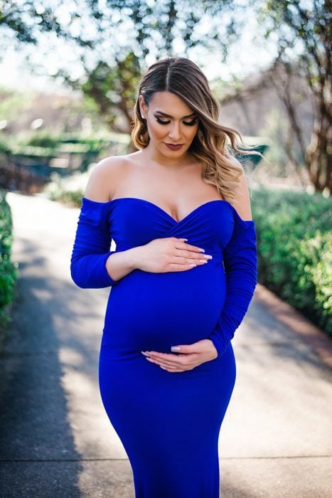 Vestidos para baby shower, mujer embarazada, con cabello castaño con mechas californianas, usando vestido azul royal sin hombros, se agarra la panza