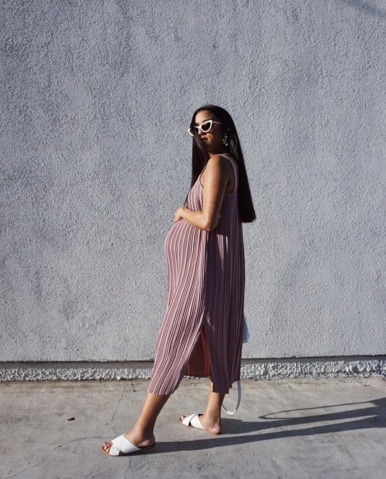 Vestidos para baby shower, mujer morena de cabello castaño, largo y lacio, embarazada y a la moda, con vestido rosa de tablas, midi y sandalias blancas abiertas