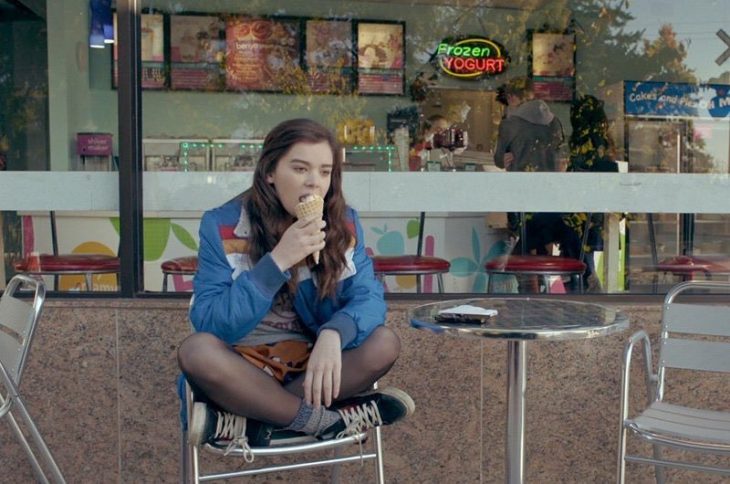 Chica sentada sola afuera de una tienda mientras come un helado