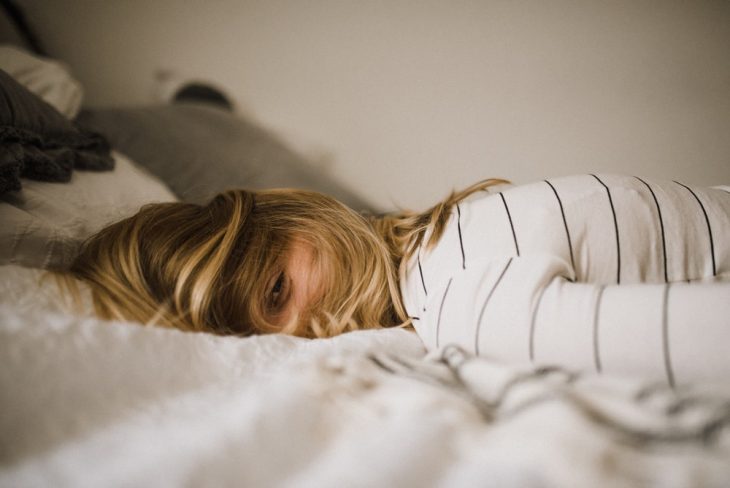 Chica con blusa blanca, líneas oscuras, recostada en una cama de sabanas blancas, haciendo prueba para entrar a La NASA y ganar 19 mil dólares