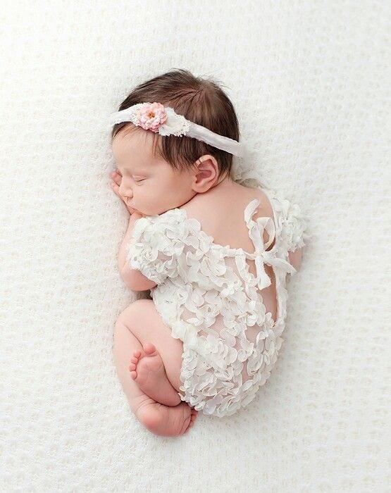 New born con temática de encaje bebé niña acotada de lado sobre una sabana blanca