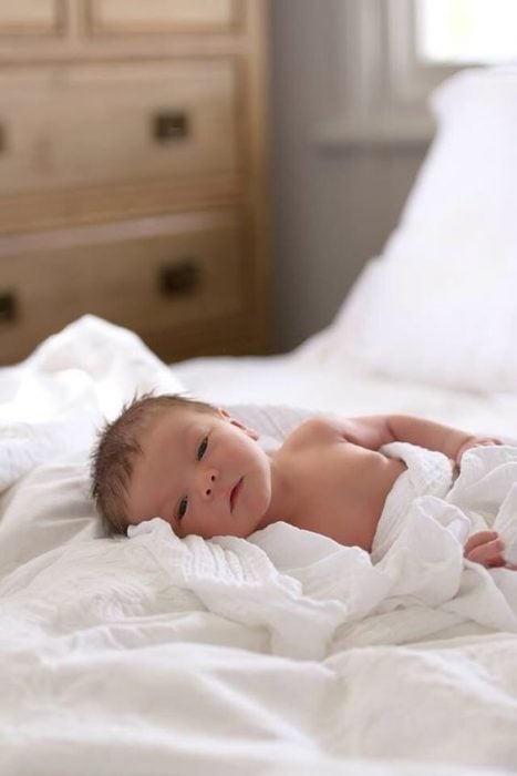 Bebé envuelto en sabanas blancas acostado en la cama