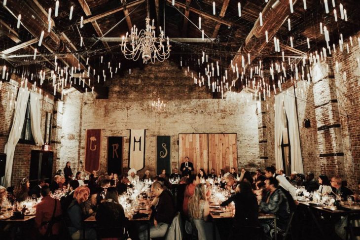 Novios se casan en boda inspirada en Harry Potter; comedor adornado como Hogwarts, con velas colgando del techo y un gran candelabro; invitados comiendo en las mesas