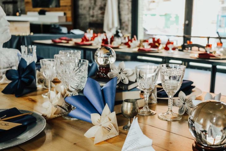 Novios se casan en boda inspirada en Harry Potter; mesa adornada con copas, libros, bola de nieve y flores de papel