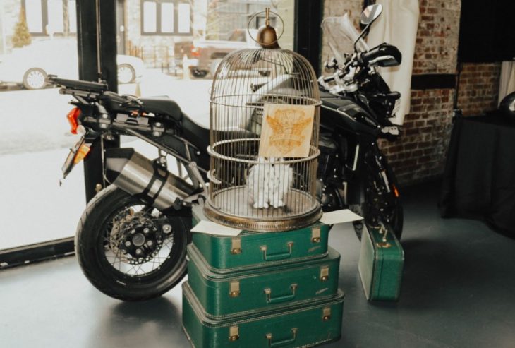 Novios se casan en boda inspirada en Harry Potter; jaula con lechuza blanca Hedwig, sobre maletas verdes y la motocicleta de Sirius Black