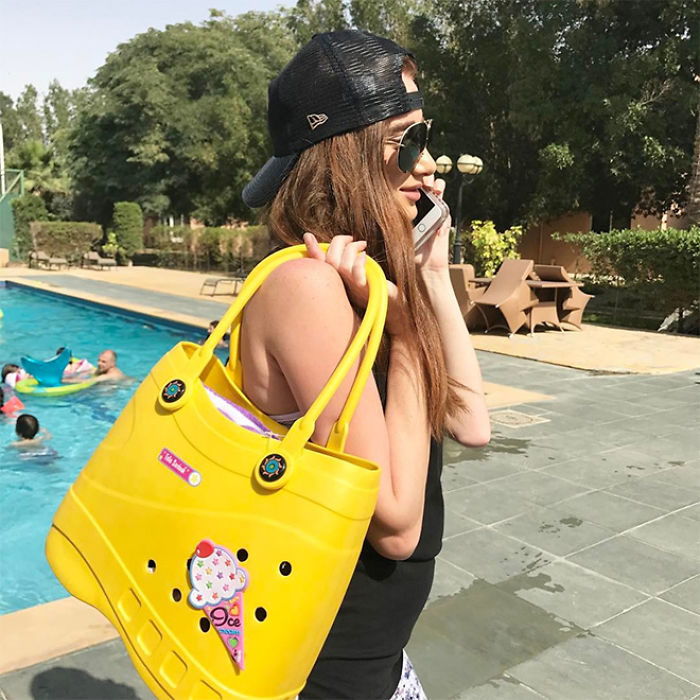 Chica hablando por celular mientras presume su bolsa Crocs en tono amarillo y con un helado que la adorna 