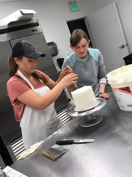 Emily Athey en compañía de una mujer decorando pasteles 