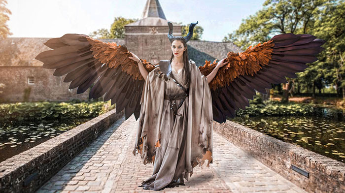 Chica vestida de Maléfica con sus enormes alas caminando por un enorme castillo 