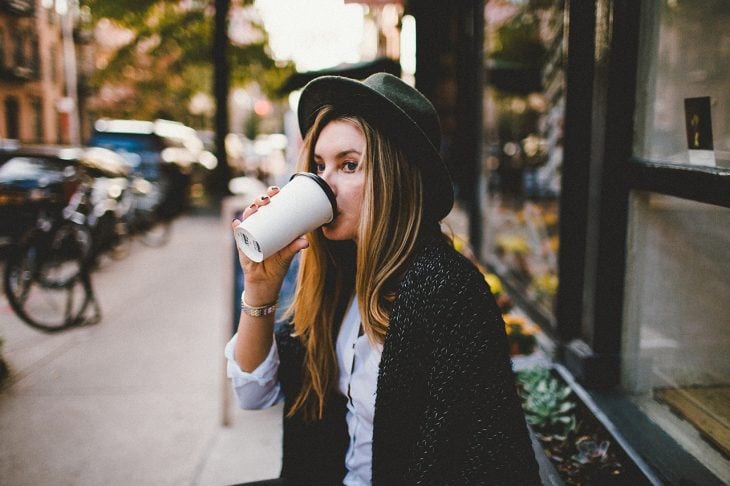 mujer bebiendo café caliente fuera de la cafetería 