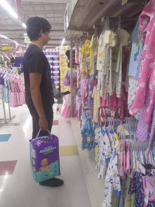 Chico parado frente a la ropa de bebé en un supermercado 