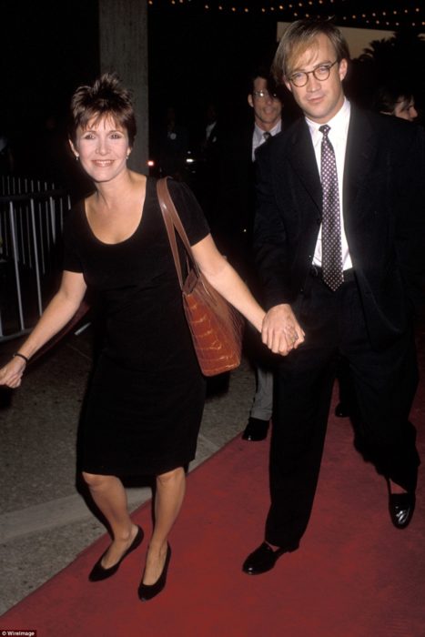 Carrie Fisher y Bryan Lourd tomados de las manos caminando por una alfombra roja 