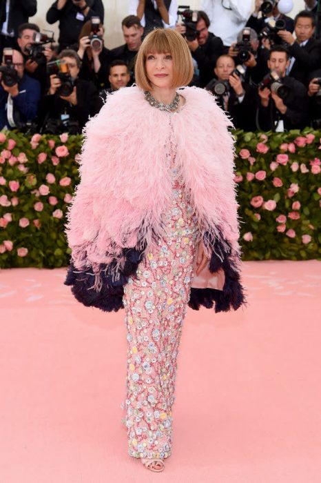 Anna Wintour, editora de Vogue Us, en la gala del MET usando un vestido rosa de lentejuelas con una capa de plumas en color rosa y morado 