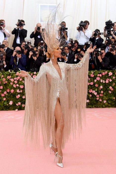 Celine Dion usando un vestido dorado con piedras y un recogido bajo con un tocado de plumas mientras posa para los fotógrafos del Met Gala