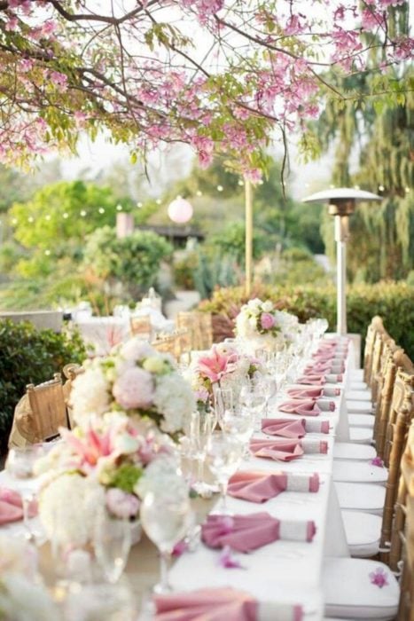 Ideas para fiesta de XV años con temática japonesa; mesa en un jardín adornada con flores y servilletas rosas