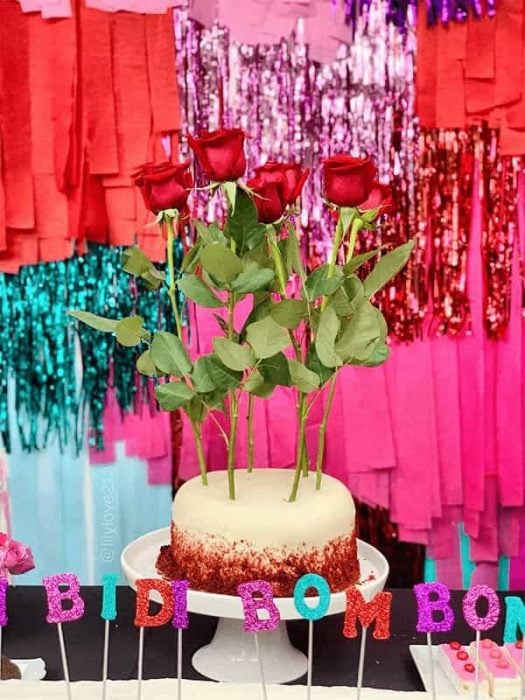 Pastel de una mesa de postres decorado con rosas y velas que dicen bidi bom bom 