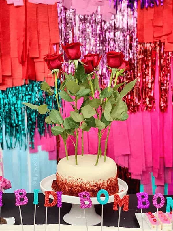 Cake of a dessert table decorated with roses and candles that say bidi bom bom 