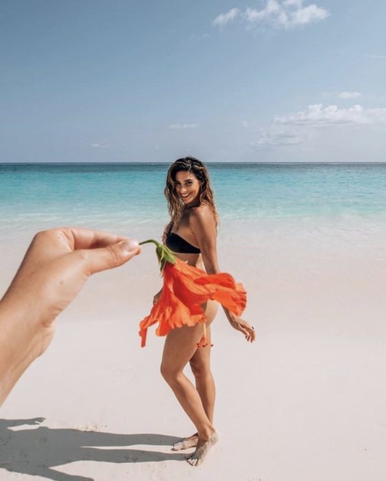 Chica tomando una foto a otra mientras le coloca una flor que da el efecto de que es una falda 