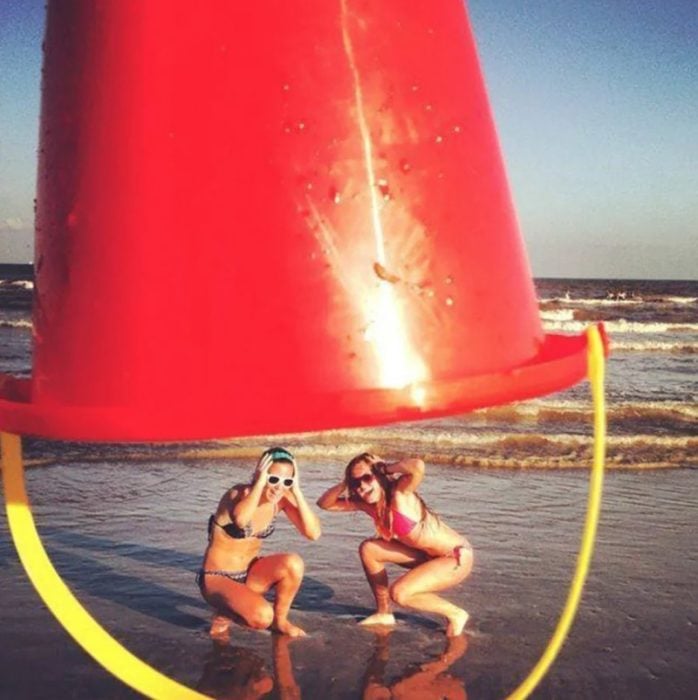 Fotos de mejores amigas; chicas intentando escapar de ser tapadas con un bote gigante mientras están en la playa 