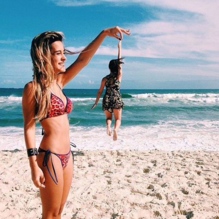 Mejores amigas en la playa tomándose una foto en la que simulan estar sosteniéndose de la mano