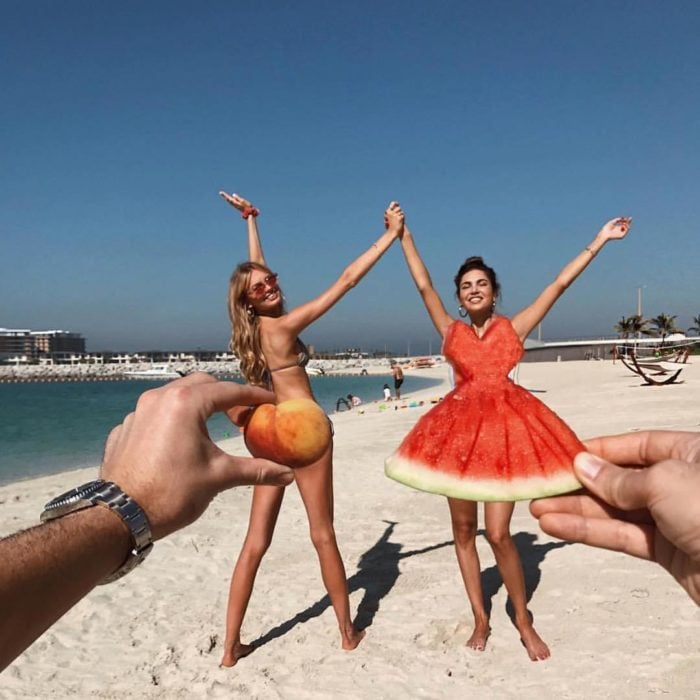 Chicas posando en la playa con un durazno que da la ilusión de ser un traje de baño y una sandía cortado como si fuera un vestido 