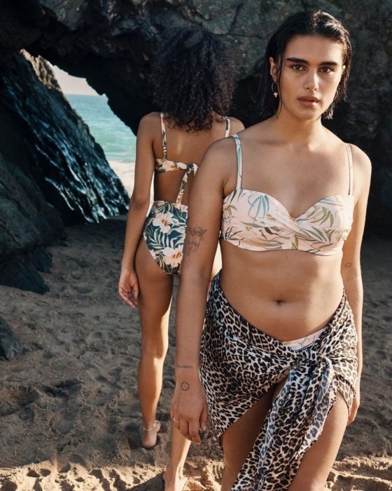 Mujer curvilínea y con tatuajes en el brazo, en la playa en traje de baño floreado y de animal print, modelando para la marca de ropa H&M