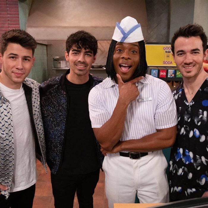 Kevin, Jeo y Nick Jonas junto a Kel Mitchell sonriendo para una fotografía dentro de un ser decorado como restaurante de hamburguesas