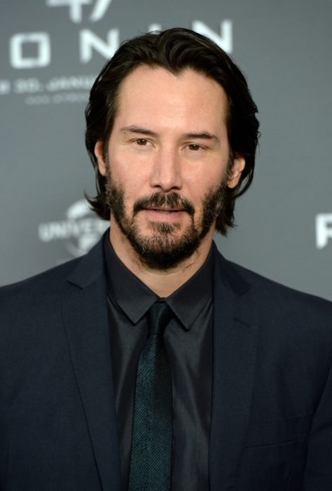 Actor Keanu Reeves, hombre con traje negro, cabello largo y corbata