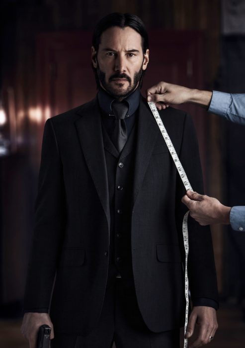 Actor Keanu Reeves, película John Wick, persona midiendo su traje negro; hombre con cabello negro, largo y barba