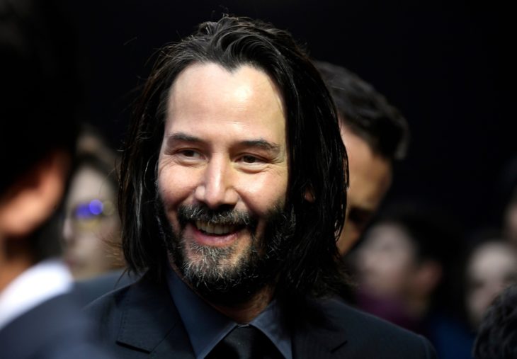 Actor Keanu Reeves, hombre con cabello negro largo, barba, bigotes y con traje