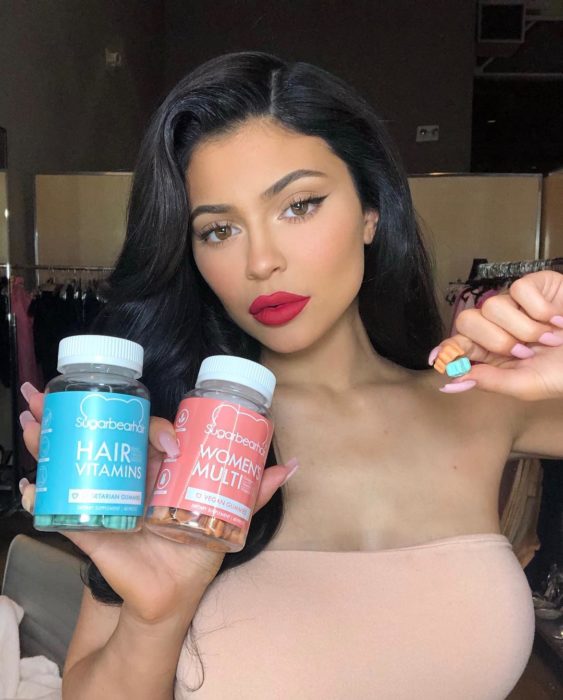 Kylie Jenner con cabello lacio sosteniendo vitaminas de gomita para el cabello y la piel en forma de oso, Sugar bear hair