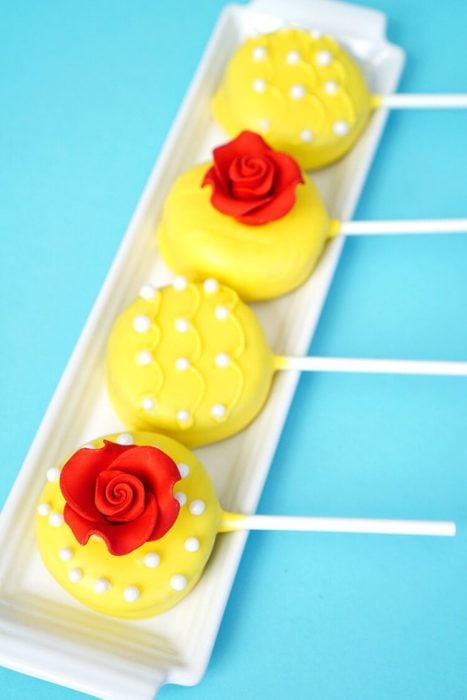 Ideas para quinceañera estilo La Bella y la Bestia de Disney; dulces, galletas cubiertas de chocolate amarillo con adornos de rosas y perlas 