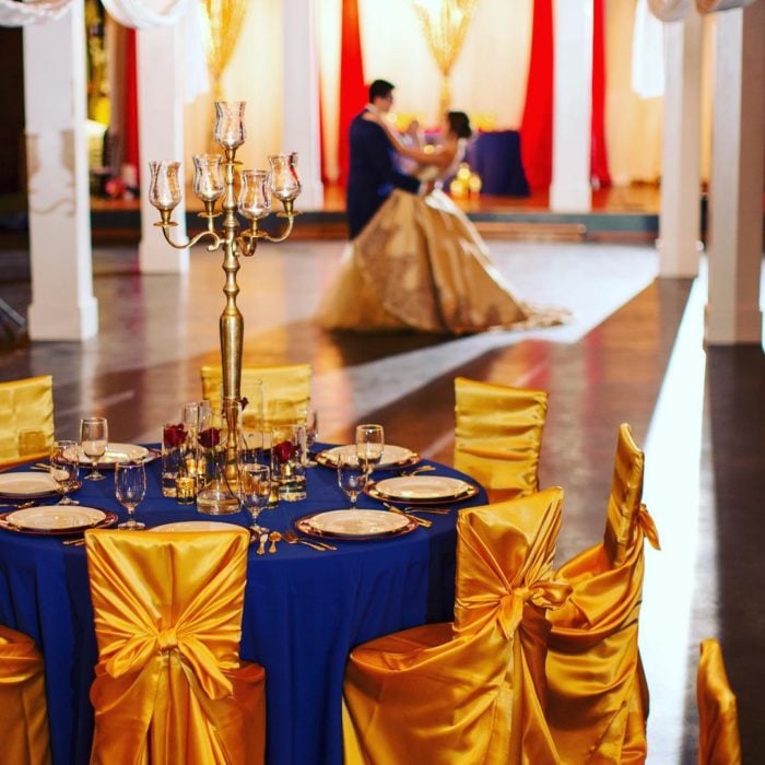 Ideas para quinceañera estilo La Bella y la Bestia de Disney; mesa adornada con mantel azul rey y sillas doradas; pareja bailando