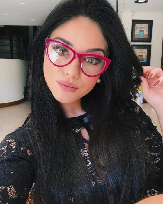 Chica posando para una selfie mientras enseña sus lentes de color rosa 