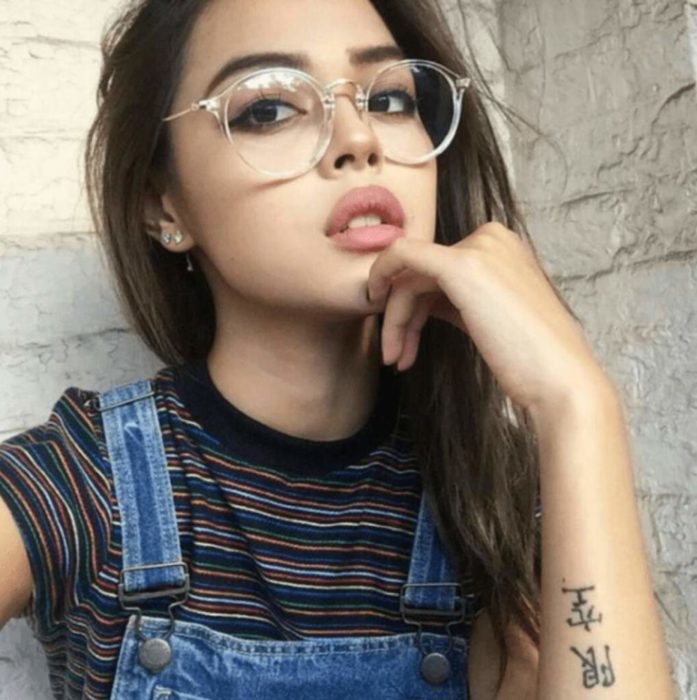 Chica posando para una foto mientras enseña sus pequeños lentes redondos y transparentes