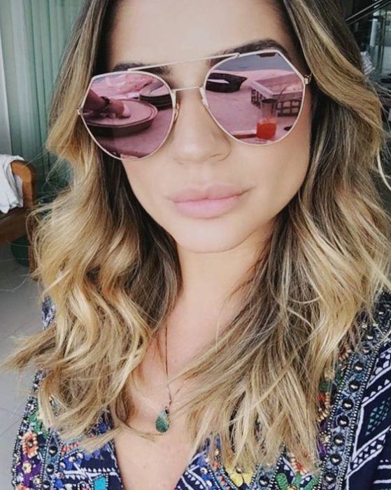 Chica tomándose una selfie con sus gafas grandes de color rosa en efecto espejo 