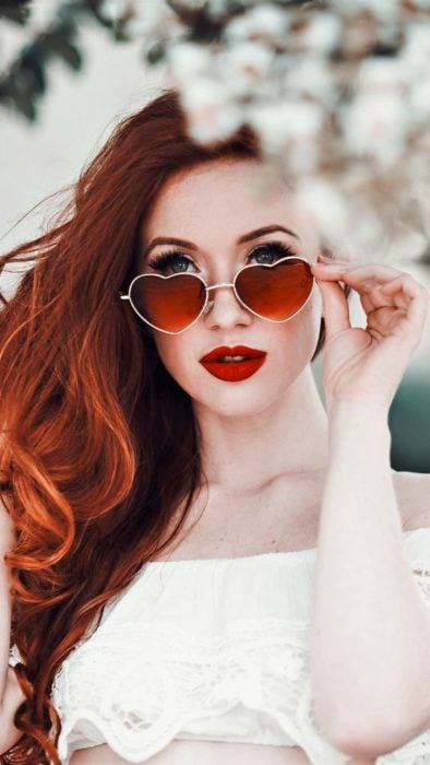 Chica modelando un par de gafas rojas con armazón en forma de corazón
