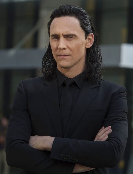 Actor Tom Hiddleston como Loki, hermano de Thor en Avengers, Marvel, hombre de cabello largo y oscuro con traje negro y cruzando los brazos