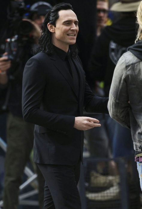 Actor Tom Hiddleston como Loki, hermano de Thor en Avengers, Marvel, hombre de cabello largo y negro en traje, caminando en la calle