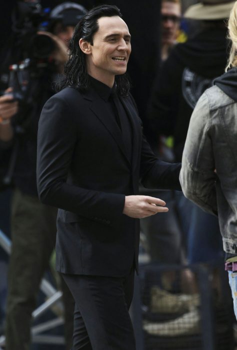 Actor Tom Hiddleston como Loki, hermano de Thor en Avengers, Marvel, hombre de cabello largo y negro en traje, caminando en la calle