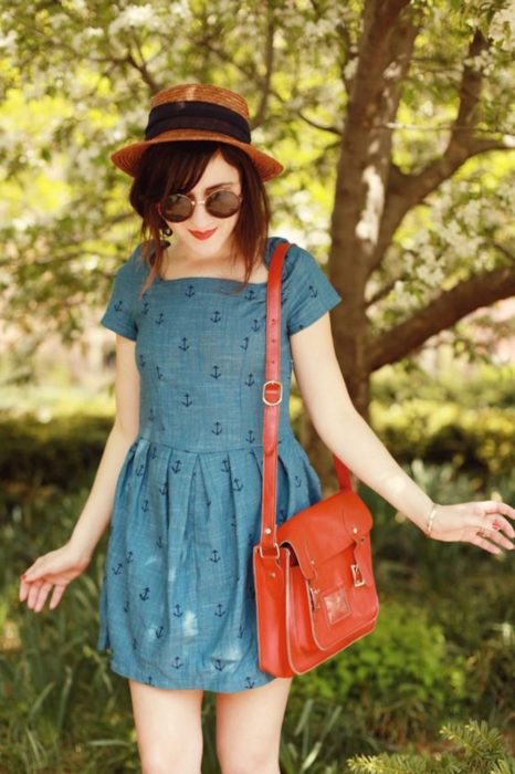 Looks de primavera; chica con vestido azul con anclas, de tela tipo mezclilla, con sombrero, lentes redondos y bolsa roja