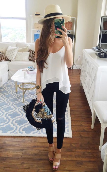 Looks de primavera; chica tomando selfie en su cuarto frente al espejo, con sombrero, blusa blanca sin mangas, pantalón de mezclilla negro y bolso de mano vintage