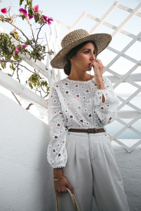 Looks de primavera; chica con rostro preocupado usando sombrero grande de mimbre, con blusa de encaje blanco con formas de estrellas y pantalón a la cintura blanco con cinto café