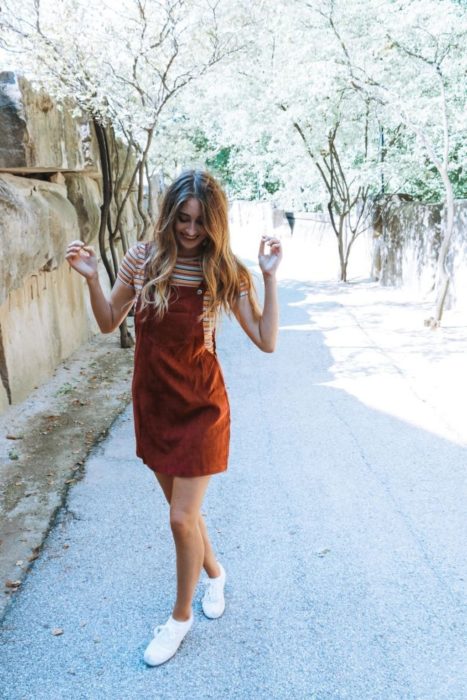 Looks de primavera; chica rubia sonriendo con overol rojo anaranhado sobre una blusa de rayas y tenis blancos