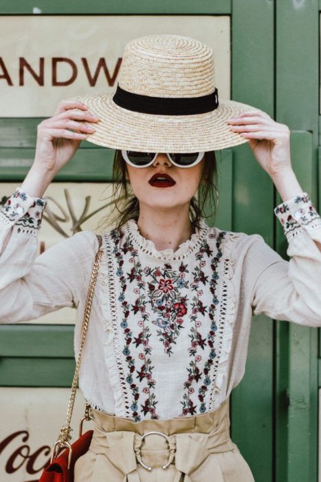 Looks de primavera; chica con sombrero de mimbre, blusa con olanes y flores bordadas, con lentes blancos y labial rojo vino