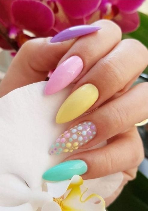 Manos de mujer con uñas estilo stiletto pintadas de colores pastel, lila, rosa, amarillo, verde