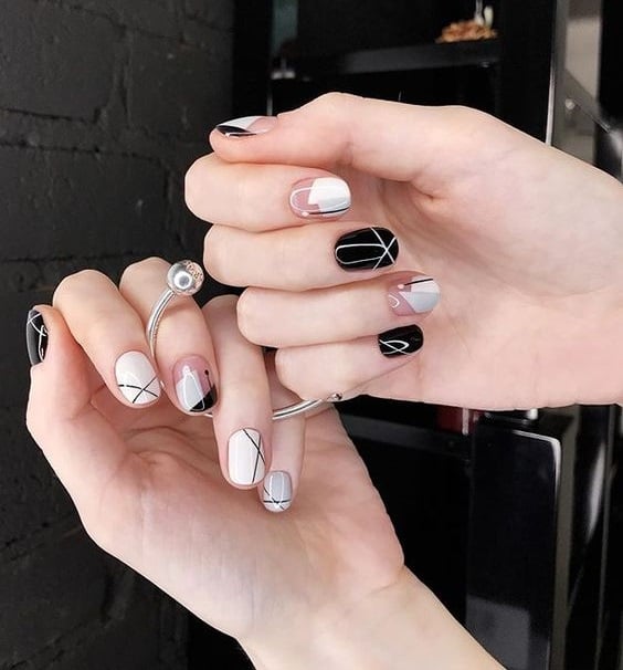 Manos de mujer con uñas redondeadas y pintandas en colores oscuros y grises