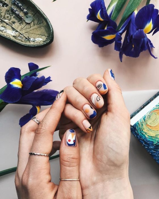 Manos de mujer sobre una mesa decorada con flores y con la uñas pintadas en figuras de colores