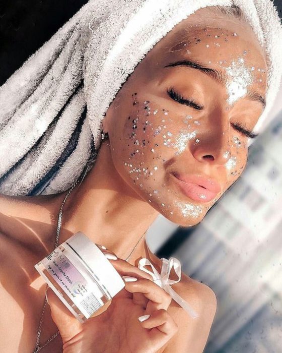 Chica con una toalla sobre la cabeza, usando mascarilla facial con estrellas y glitters 