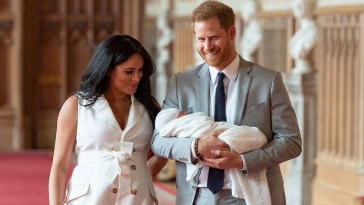 Meghan Markle y el príncipe Harry abrazados de manera lateral, sosteniendo a su bebé en brazos 