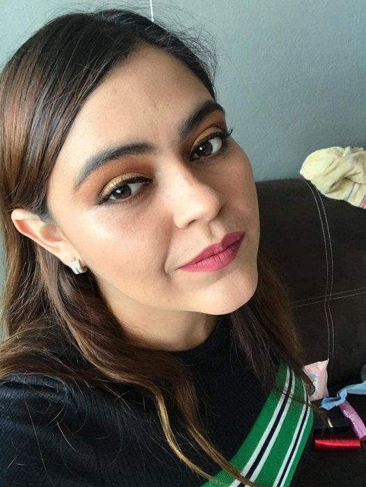 Chica ayuda a su mejor amiga a maquillarse vía Whatsapp; selfie de joven con maquillaje bonito de día, sombras anaranjada y amarilla, delineado cat eye y labial rosa